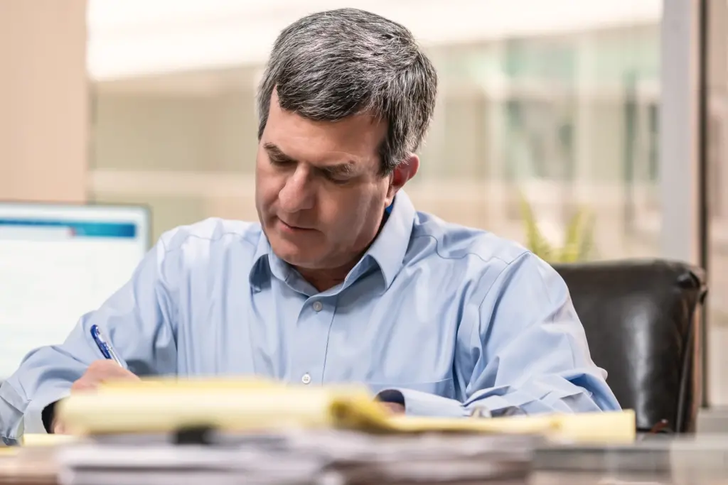 Close up of Sandford working in his office and writing notes on a note pad.