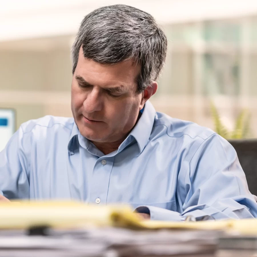 Close up of Sandford working in his office and writing notes on a note pad.